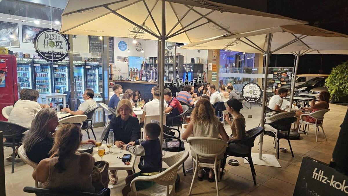 Terraza nocturna de Rock N Hopz con gente compartiendo cerveza y comida